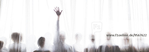 Silhouette von Menschen hinter transparentem Vorhang,  eine Person hebt die Hand