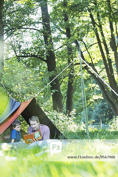 Vater und Sohn lesen im Campingzelt