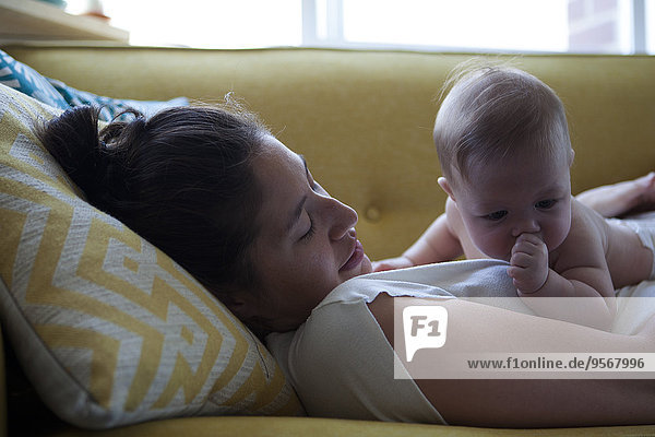 View of mother lying on sofa with little baby sucking thumb