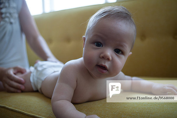 Porträt des kleinen Babys auf dem gelben Sofa liegend  mit Blick auf die Kamera