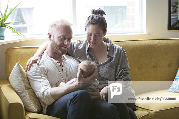 Eltern lächelnd und haltend kleines Baby  sitzend auf gelbem Sofa