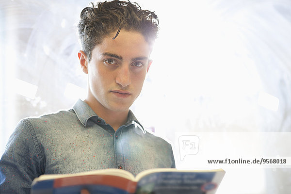 Portrait of university student with book standing beside window
