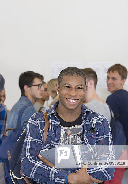 Male student holding books and smiling at camera with other students in background