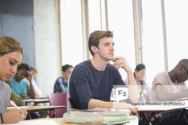 Male student with hand on chin during lecture with other students in background