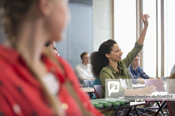 Female student raising hand during lecture with other students in background