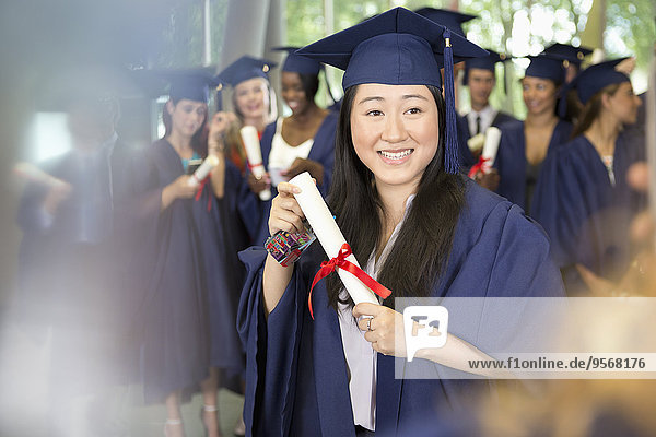 Portrait of smiling female student in graduation gown holding diploma