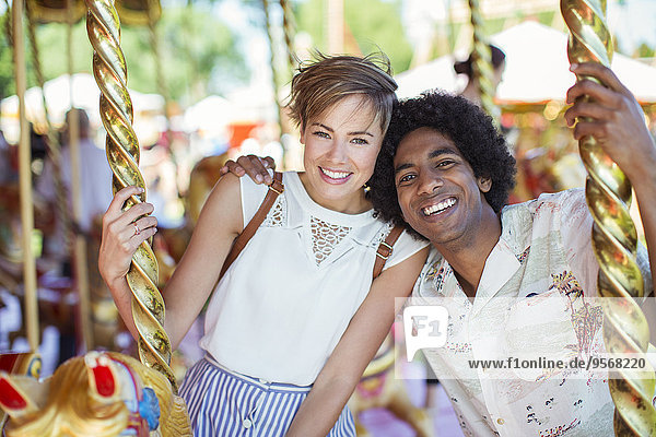 Junges multirassisches Paar lächelt auf Karussell im Vergnügungspark