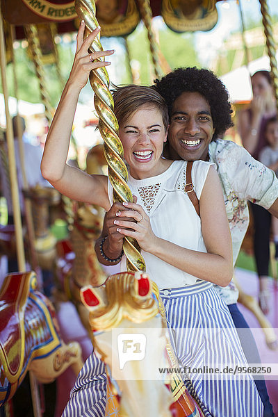 Junges multirassisches Paar lächelt auf Karussell im Vergnügungspark