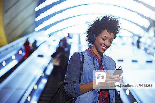 Lächelnde Frau hört mp3-Player auf Rolltreppe