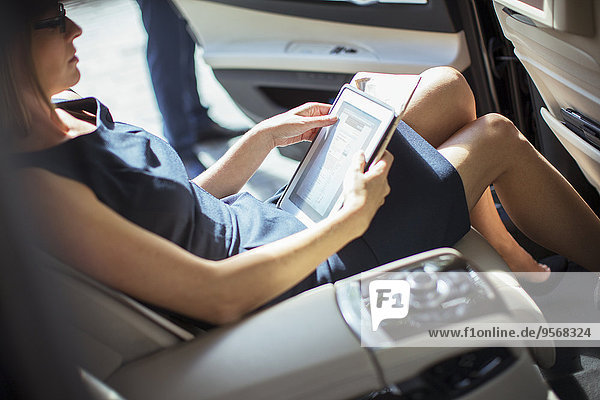 Geschäftsfrau mit digitalem Tablett auf dem Rücksitz des Autos