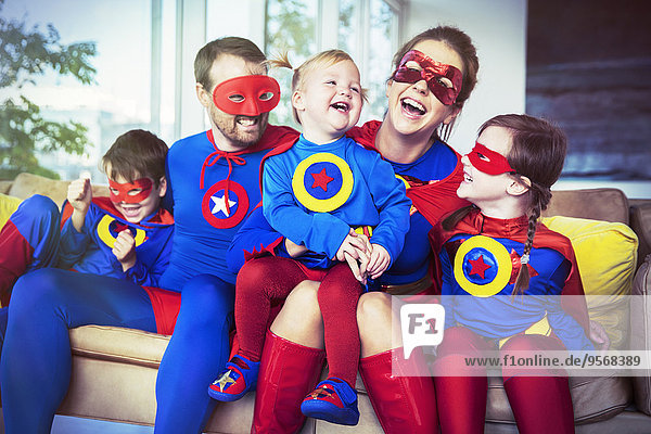Superheldenfamilie lacht auf dem Sofa