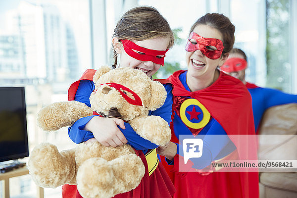 Superheldenmutter und -tochter spielen mit Teddybären