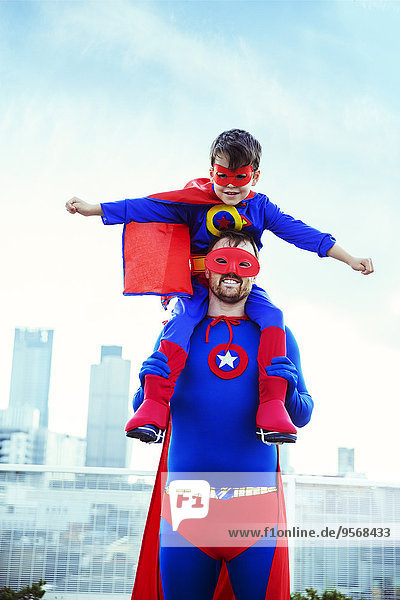 Superhelden-Vater mit Sohn auf den Schultern auf dem Dach der Stadt