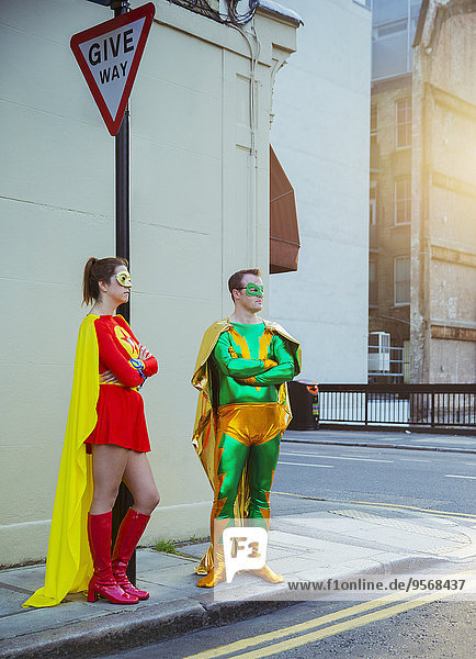 Superheldenpaar wartet an der Ecke auf dem Bürgersteig der Stadt