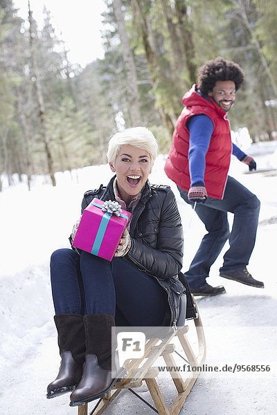 Man pulling woman with gift on sled in snow