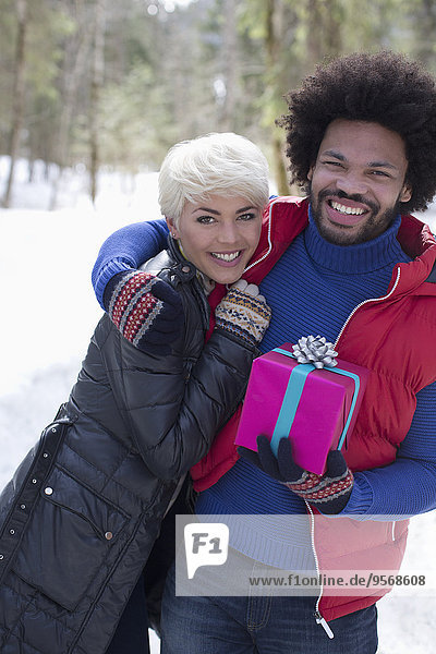 Portrait of couple with Christmas gift hugging in snow