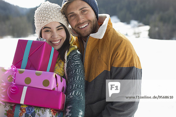 Portrait of smiling couple with Christmas gifts in snow