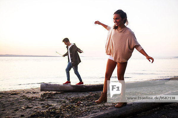Caucasian couple walking on logs on beach