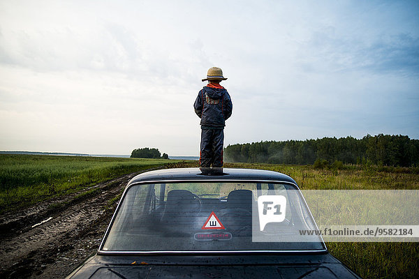 Caucasian boy standing on car roof in rural field