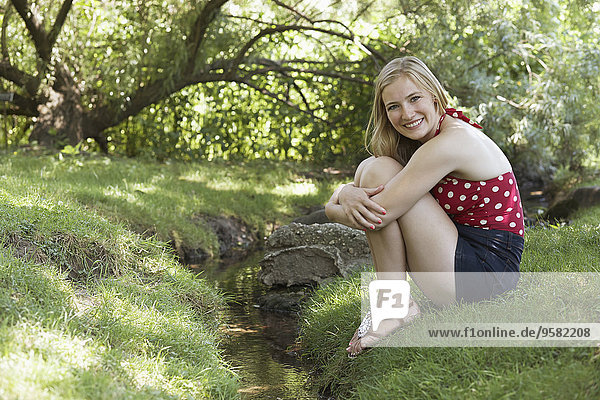 Smiling woman sitting near creek in park