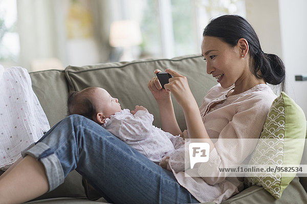 Asian mother taking cell phone photograph of baby in living room