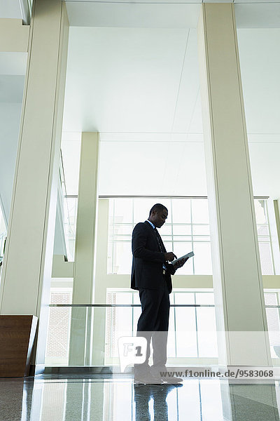 Black businessman using digital tablet in office hallway