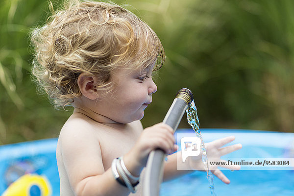 Caucasian baby boy playing with hose in swimming pool