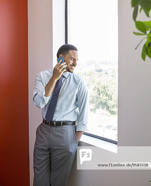 Black businessman talking on cell phone at office window