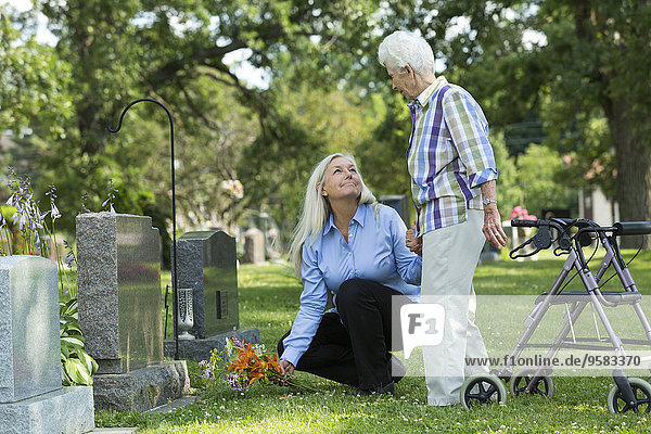 Caucasian mother and daughter visiting grave in cemetery