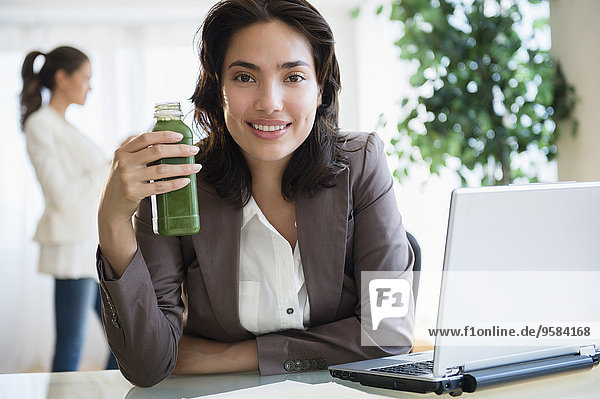 Hispanic businesswoman drinking green juice at desk in office