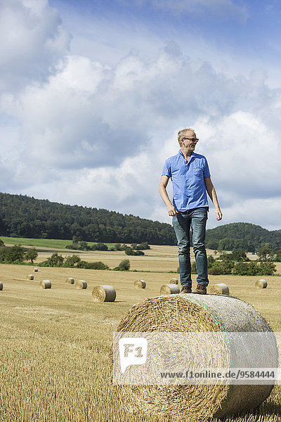 Farmer standing on hay bale in field