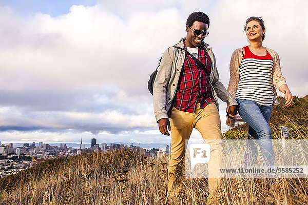 Couple walking on grassy hill overlooking cityscape