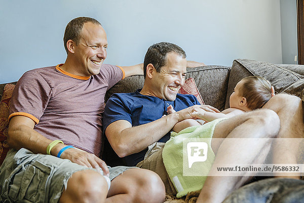 Caucasian gay couple playing with baby boy on sofa