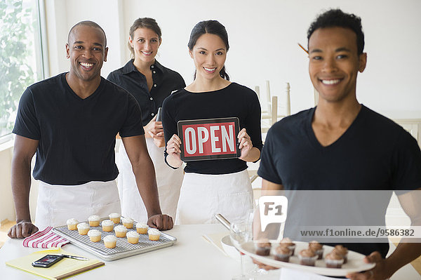 Caterers smiling together with food and open sign in event space
