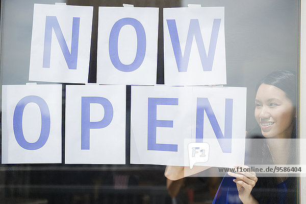 Woman hanging now open sign in store window