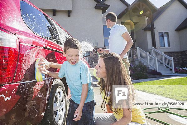 Caucasian family washing car in driveway