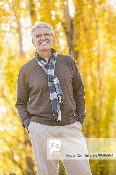 Older Caucasian man smiling near autumn trees