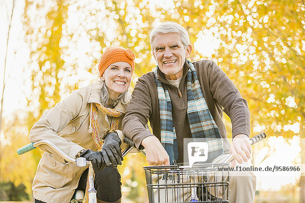 Older Caucasian couple riding bicycles near autumn trees