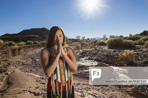 Mixed race woman praying in remote desert landscape