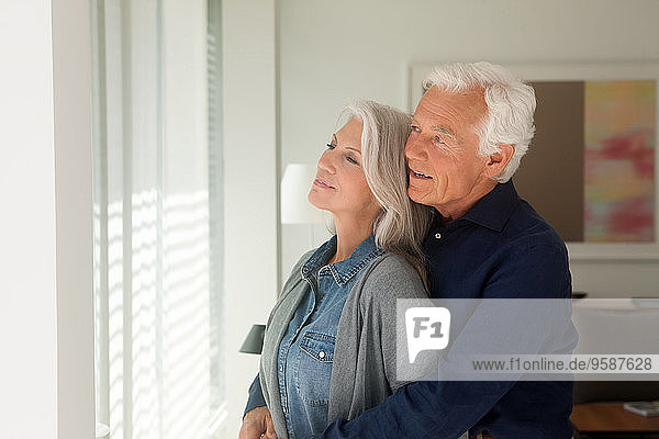 Porträt eines liebenden älteren Paares  das zusammen aus dem Fenster schaut.