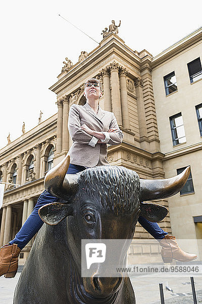 Deutschland  Hessen  Frankfurt  Geschäftsfrau mit gekreuzten Armen auf Stierskulptur vor der Börse sitzend