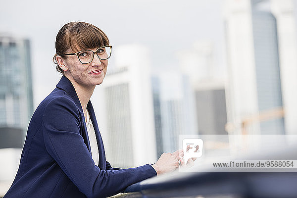 Deutschland  Hessen  Frankfurt  Porträt einer lächelnden Geschäftsfrau mit Brille und Smartphone