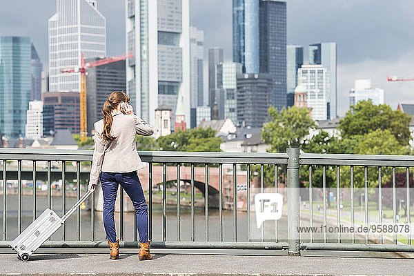 Deutschland  Hessen  Frankfurt  telefonierende Geschäftsfrau mit Rollkoffer auf einer Brücke stehend