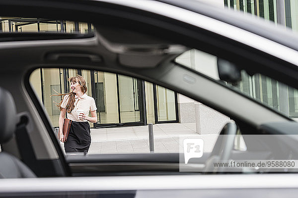 Deutschland  Hessen  Frankfurt  fröhliche Geschäftsfrau  die mit Kaffee hinter einem Auto geht.