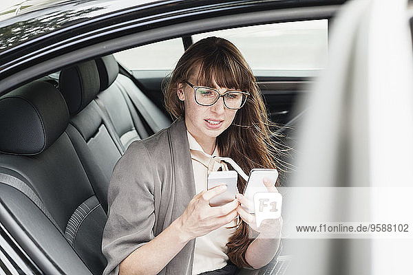 Deutschland  Geschäftsfrau im Auto sitzend mit zwei Smartphones