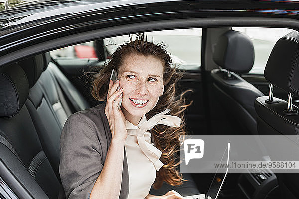 Germany  portrait of smiling businesswoman sitting in a car telephoning with smartphone