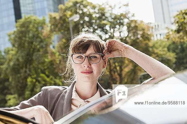 Porträt einer Geschäftsfrau  die sich auf ihr Auto stützt
