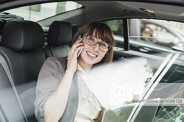 Germany  portrait of smiling businesswoman sitting in a car telephoning with smartphone