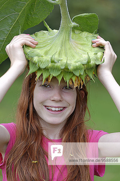 Porträt des lächelnden Mädchens mit Sonnenblumenblüte  Helianthus annuus  auf dem Kopf