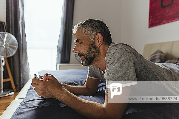 Mann auf dem Bett liegend mit seinem Smartphone